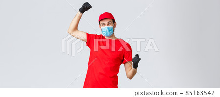 Groceries and packages delivery, covid-19, quarantine and shopping concept. Cheerful courier red uniform, gloves and face mask, raising hands up, chanting rejoicing over good news, fight coronavirus 85163542