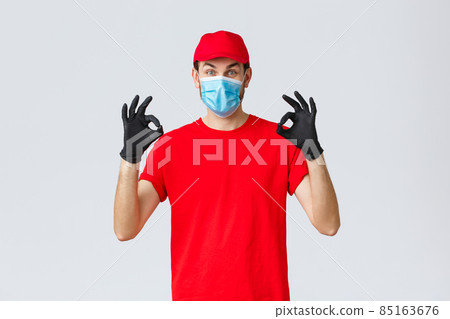 Covid-19, self-quarantine, online shopping and shipping concept. Excited delivery guy in red cap, t-shirt and face mask working coronavirus outbreak, show okay sign, guarantee safe courier service 85163676