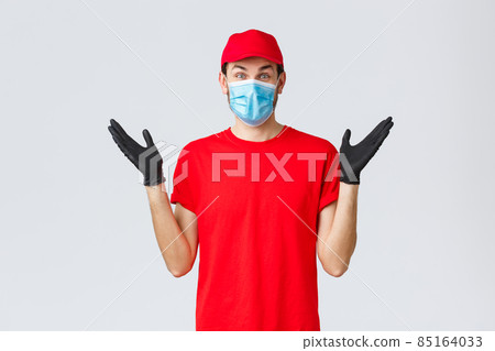 Groceries and packages delivery, covid-19, quarantine and shopping concept. Happy rejoicing delivery guy in red uniform, face mask and gloves receive good news, clap hands applause surprised Groceries and packages delivery, covid-19, quarantine and shopping concept. Happy rejoicing delivery guy in red uniform, face mask and gloves receive good news, clap hands applause surprised 85164033