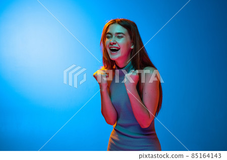 Emotional excited girl shouting isolated on blue studio backgroud in neon light. Human emotions, facial expression concept 85164143