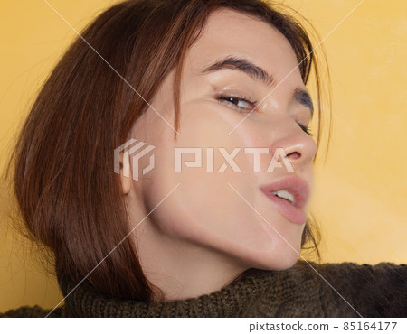 Close-up face of funny young girl crushed on glass isolated on light yellow studio background. Close-up face of funny young girl crushed on glass isolated on light yellow studio background. 85164177