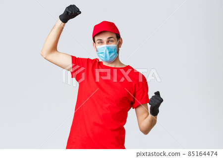Groceries and packages delivery, covid-19, quarantine and shopping concept. Cheerful courier red uniform, gloves and face mask, raising hands up, chanting rejoicing over good news, fight coronavirus Groceries and packages delivery, covid-19, quarantine and shopping concept. Cheerful courier red uniform, gloves and face mask, raising hands up, chanting rejoicing over good news, fight coronavirus 85164474
