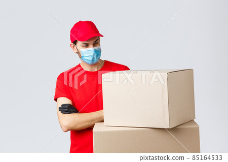 Packages and parcels delivery, covid-19 quarantine and transfer orders. Curious male courier in red uniform, medical face mask and gloves, looking interested at boxes, cross arms, stare intrigued Packages and parcels delivery, covid-19 quarantine and transfer orders. Curious male courier in red uniform, medical face mask and gloves, looking interested at boxes, cross arms, stare intrigued 85164533