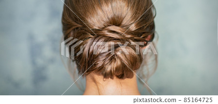 Rearview of young brunette woman with beautiful middle bun hairstyle on gray background. 85164725
