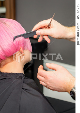 Hands of hairdresser combing hair making short pink hairstyle for a young caucasian woman in a beauty salon. 85164749