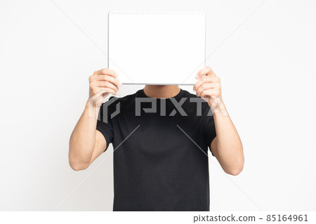 A man wearing a black T-shirt standing in front of a white background and showing a small sketchbook 85164961