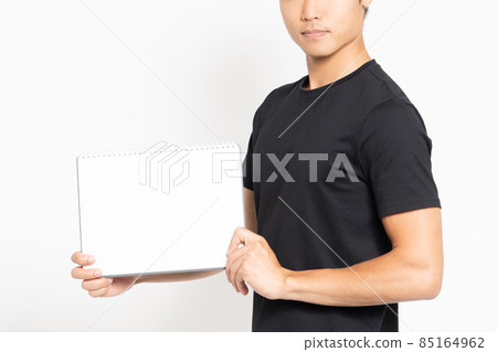 A man wearing a black T-shirt standing in front of a white background and showing a small sketchbook 85164962