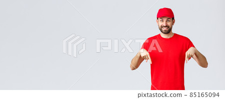 Online shopping, delivery during quarantine and takeaway concept. Cheerful friendly courier in red uniform cap and t-shirt, pointing fingers down, inform clients, recommend advertisement 85165094