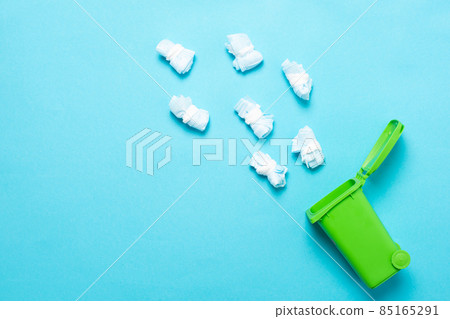 Throw away folded medical masks in a green container for recycling on a blue background. Blue face masks after use. Using medical masks Throw away folded medical masks in a green container for recycling on a blue background. Blue face masks after use. Using medical masks 85165291