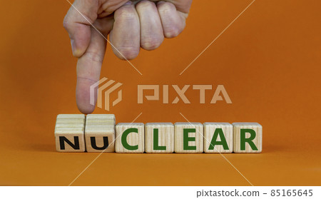 Nuclear or clear symbol. Businessman turns a cube and changes the word 'nuclear' to 'clear'. Beautiful orange background. Nuclear or clear and business concept. Copy space. 85165645