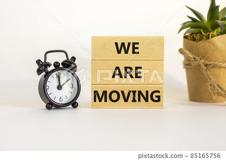 We are moving symbol. Wooden blocks with words 'We are moving'. Beautiful white background, black alarm clock, house plant. Business, we are moving concept, copy space. 85165756