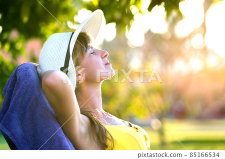 Young woman relaxing outdoors on sunny summer day. Happy lady lying down on comfortable beach chair daydreaming thinking. Calm beautiful smiling girl enjoying fresh air relaxing with closed eyes. Young woman relaxing outdoors on sunny summer day. Happy lady lying down on comfortable beach chair daydreaming thinking. Calm beautiful smiling girl enjoying fresh air relaxing with closed eyes. 85166534