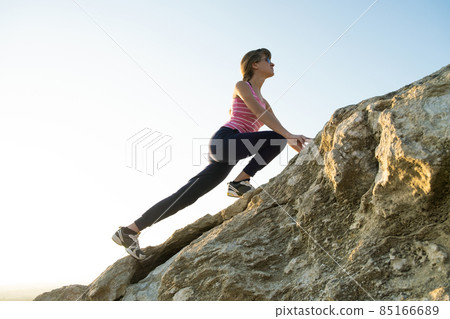 Woman hiker climbing steep big rock on a sunny day. Young female climber overcomes difficult climbing route. Active recreation in nature concept. 85166689