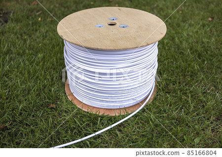 Top view of roll of white industrial electrical cable on large wooden reel isolated outdoors on green grass. Professional construction site cable, reliable wiring and durability. Top view of roll of white industrial electrical cable on large wooden reel isolated outdoors on green grass. Professional construction site cable, reliable wiring and durability. 85166804