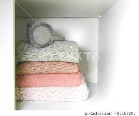 White shelf of the home wardrobe with colorful sweaters, jumpers and warm headphones. Small space organization White shelf of the home wardrobe with colorful sweaters, jumpers and warm headphones. Small space organization 85167295
