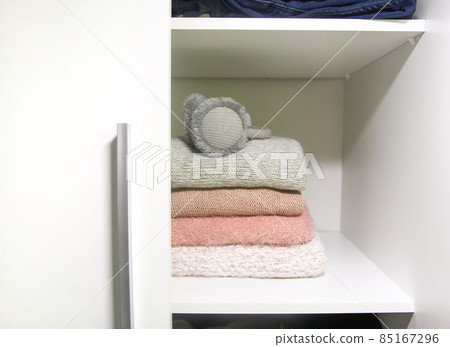 White shelf of the home wardrobe with colorful sweaters, jumpers and warm headphones. Small space organization White shelf of the home wardrobe with colorful sweaters, jumpers and warm headphones. Small space organization 85167296