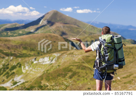 Male hiker standing on top of the rocky peak overlooking mountain landscape. 85167791