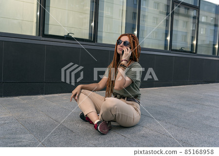 Young woman in black glasses sits against the background of an office building and talks on the phone. Lotus pose Young woman in black glasses sits against the background of an office building and talks on the phone. Lotus pose 85168958