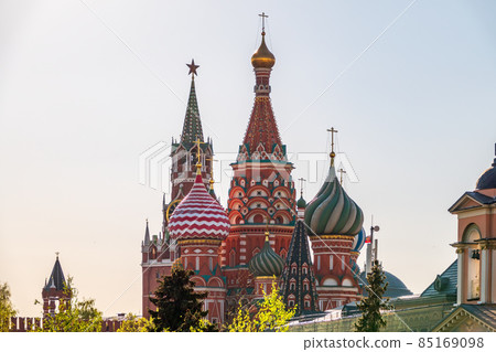 Multi-colored domes of St. Basil's Cathedral and the Spasskaya Tower of the Moscow Kremlin around the trees. Symbols of the Russian state. Multi-colored domes of St. Basil's Cathedral and the Spasskaya Tower of the Moscow Kremlin around the trees. Symbols of the Russian state. 85169098