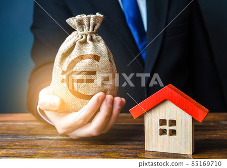 Man holds out a euro bag near the house. Bank approval for issuing a mortgage loan. Home purchase, invest in real estate. Property appraisal. Favorable terms and conditions, low interest rate. 85169710