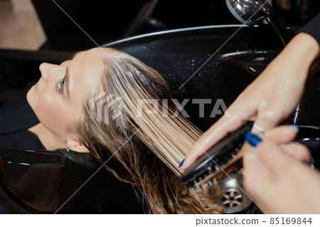 Hairdresser in beauty salon washes his client hair, before procedure of applying natural restoring ingredients and vitamins to hair and haircut. 85169844
