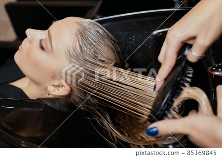 Hairdresser in beauty salon washes his client hair, before procedure of applying natural restoring ingredients and vitamins to hair and haircut. 85169845