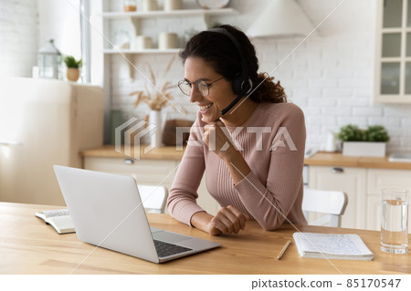 Smiling woman in headset working online, looking at laptop screen 85170547