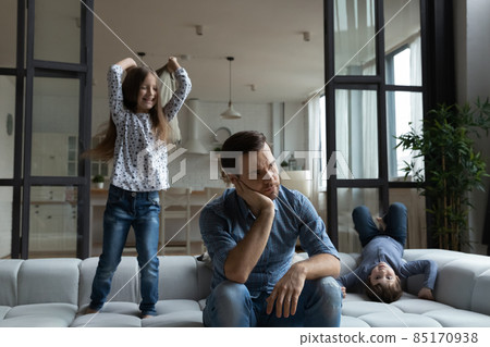 Tired father sitting on couch with noisy daughter and son 85170938