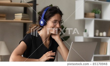 Smiling Latin woman in headphones talk on video call Smiling Latin woman in headphones talk on video call 85170948