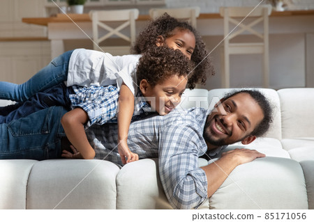 African children piled on their father lying on sofa indoor African children piled on their father lying on sofa indoor 85171056