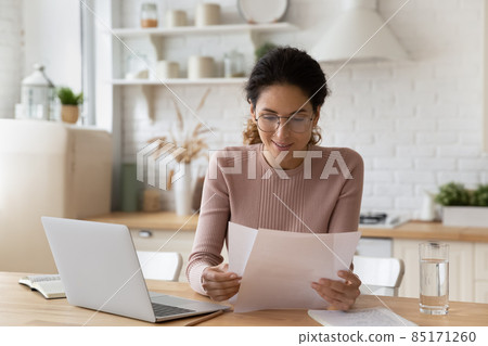 Smiling woman in glasses working with documents, using laptop Smiling woman in glasses working with documents, using laptop 85171260