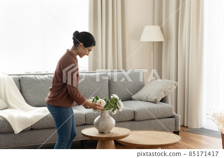 Smiling young indian ethnicity woman putting flowers in vase. 85171417