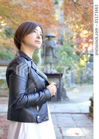 A smiling young woman with short hair posing against the backdrop of autumn leaves 85171663