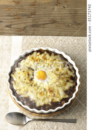 A bird's-eye view of a freshly baked curry and a spoon with plenty of melted cheese and eggs on it A bird's-eye view of a freshly baked curry and a spoon with plenty of melted cheese and eggs on it 85173740