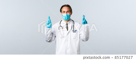 Covid-19, preventing virus, healthcare workers and vaccination concept. Optimistic hopeful doctor praying for patients lives, end of coronavirus, cross fingers making wish, wear medical mask. Covid-19, preventing virus, healthcare workers and vaccination concept. Optimistic hopeful doctor praying for patients lives, end of coronavirus, cross fingers making wish, wear medical mask. 85177027