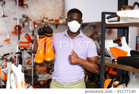 Man wearing protective mask chooses rubber boots at garden supply store Man wearing protective mask chooses rubber boots at garden supply store 85177140