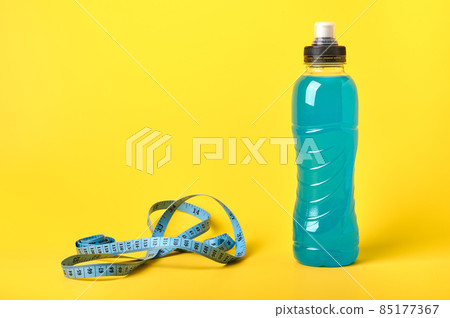 Isotonic energy blue transparent sport drink in plastic bottle and measure tape on yellow background Isotonic energy blue transparent sport drink in plastic bottle and measure tape on yellow background 85177367