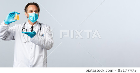 Covid-19, preventing virus, healthcare workers and vaccination concept. Pleased smiling doctor in medical mask and gloves show urine sample, satisfied with clean test result, white background 85177472