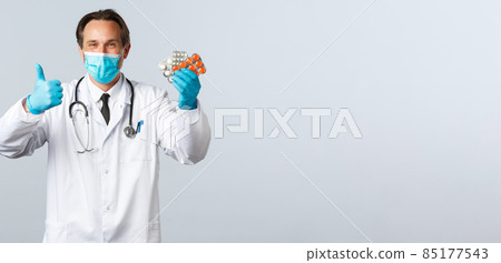 Covid-19, preventing virus, healthcare workers and vaccination concept. Satisfied handsome doctor smiling, wear medical mask and gloves, thumb-up as recommend pills, show good medication Covid-19, preventing virus, healthcare workers and vaccination concept. Satisfied handsome doctor smiling, wear medical mask and gloves, thumb-up as recommend pills, show good medication 85177543