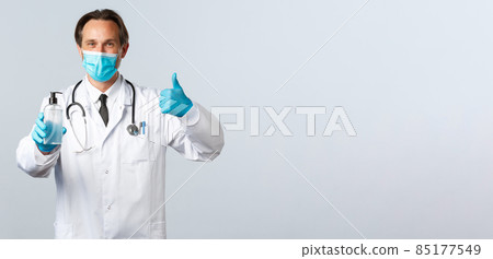 Covid-19, preventing virus, healthcare workers and vaccination concept. Satisfied doctor in medical mask and gloves thumb-up in approval, recommend hand sanitizer, white background 85177549