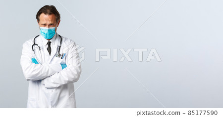 Covid-19, preventing virus, healthcare workers and vaccination concept. Offended timid doctor in medical mask and gloves looking insulted and upset, cross hands chest and frowning gloomy Covid-19, preventing virus, healthcare workers and vaccination concept. Offended timid doctor in medical mask and gloves looking insulted and upset, cross hands chest and frowning gloomy 85177590