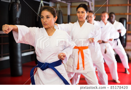 Adults in kimono trying new martial moves at karate class in gym 85178420