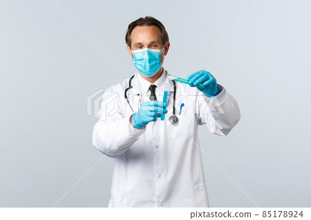 Covid-19, preventing virus, healthcare workers and vaccination concept. Smiling doctor in medical mask and gloves pouring chemical ingridient into another test-tube, conducting vaccine tests 85178924