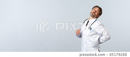 Covid-19, coronavirus outbreak, healthcare workers and pandemic concept. Troubled middle-aged male doctor feeling exhausted after night shift at clinic with sick patients, sprained back Covid-19, coronavirus outbreak, healthcare workers and pandemic concept. Troubled middle-aged male doctor feeling exhausted after night shift at clinic with sick patients, sprained back 85179288