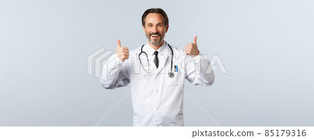 Covid-19, coronavirus outbreak, healthcare workers and pandemic concept. Satisfied cheerful male doctor in white coat showing thumbs-up in approval. Therapist recommend medication Covid-19, coronavirus outbreak, healthcare workers and pandemic concept. Satisfied cheerful male doctor in white coat showing thumbs-up in approval. Therapist recommend medication 85179316