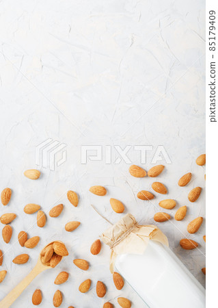 Almond milk in a glass bottle on a light background with a scattering of seed kernels and a wooden spoon. Almond milk in a glass bottle on a light background with a scattering of seed kernels and a wooden spoon. 85179409
