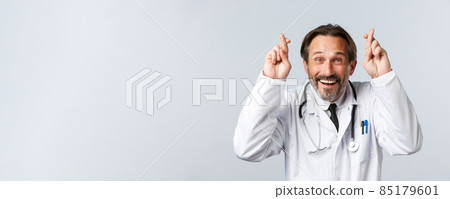 Covid-19, preventing virus, healthcare workers and vaccination concept. Close-up of optimistic hopeful doctor in white coat, cross fingers good luck and smiling, having faith, making wish 85179601