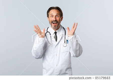 Covid-19, coronavirus outbreak, healthcare workers and pandemic concept. Excited happy male doctor telling great news, raising hands up and smiling thrilled, reacting to awesome promo Covid-19, coronavirus outbreak, healthcare workers and pandemic concept. Excited happy male doctor telling great news, raising hands up and smiling thrilled, reacting to awesome promo 85179683