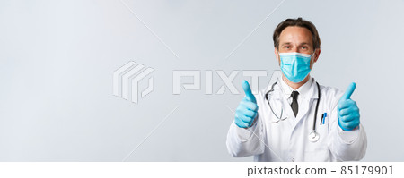 Covid-19, preventing virus, healthcare workers and vaccination concept. Close-up of pleased doctor in medical mask and gloves, show thumbs-up, guarantee quality of provided service, recommend product 85179901