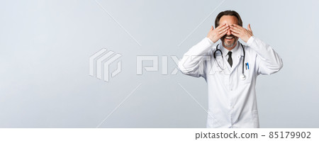 Covid-19, coronavirus outbreak, healthcare workers and pandemic concept. Surprised happy male doctor in white coat close eyes with hands and waiting, anticipating surprise, white background 85179902